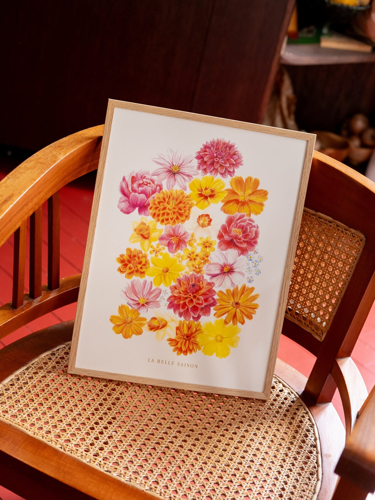 ffiche de fleurs colorées « La Belle Saison », présentée dans un cadre en bois clair sur une chaise cannée.