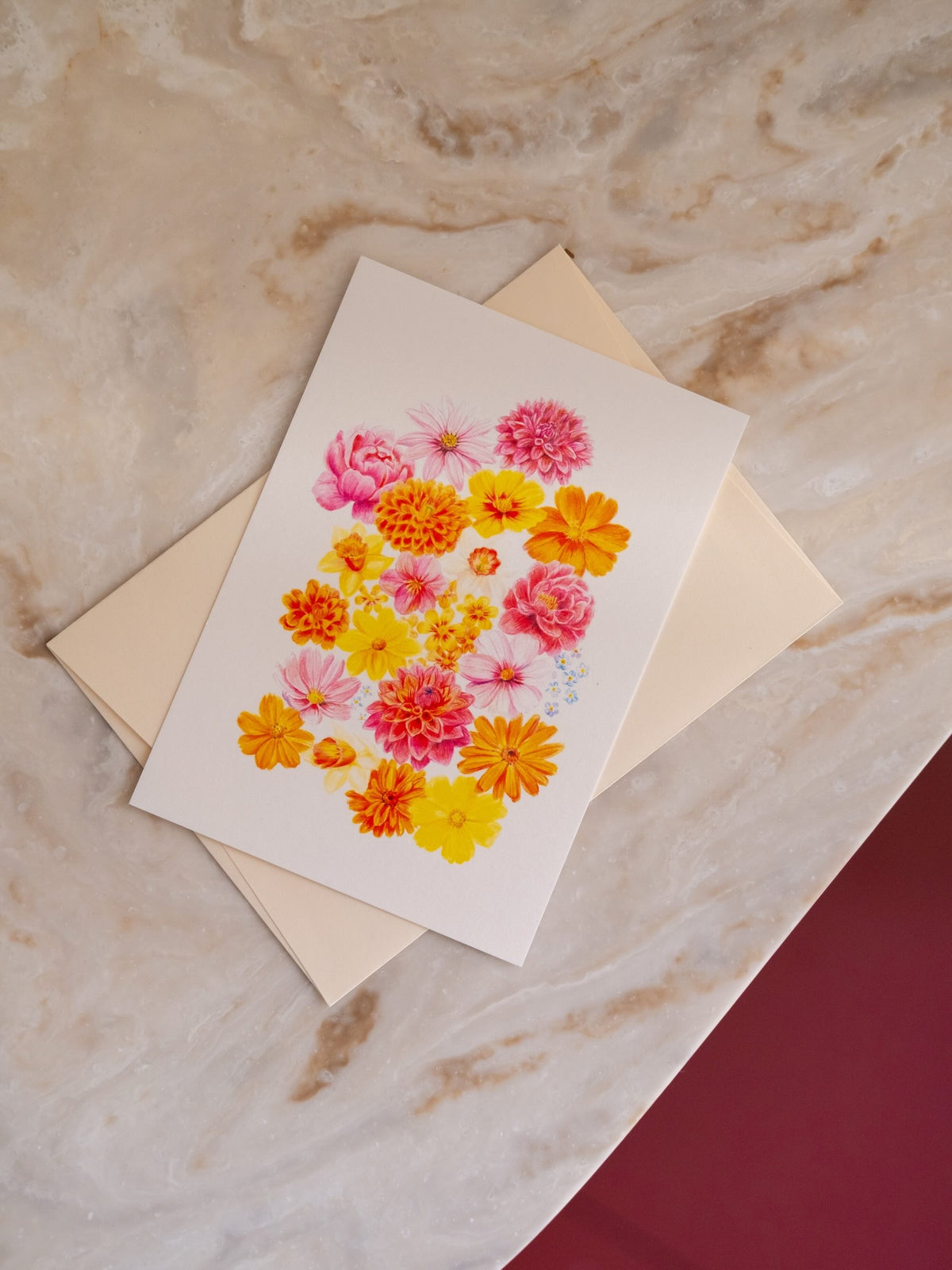Carte postale florale « La Belle Saison », aux fleurs roses, jaunes et orange, posée sur une enveloppe sur du marbre clair.
