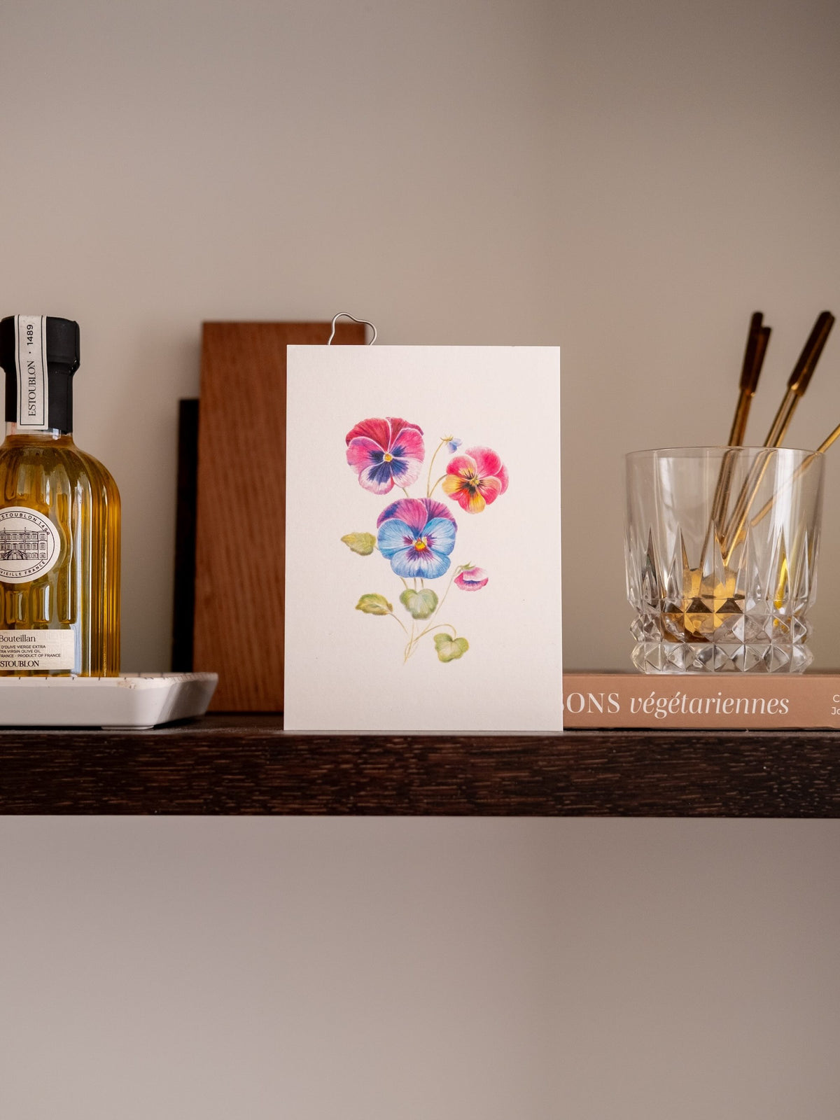 Carte postale florale Pensées, illustrée de fleurs roses, violettes et bleues, présentée debout sur une étagère.