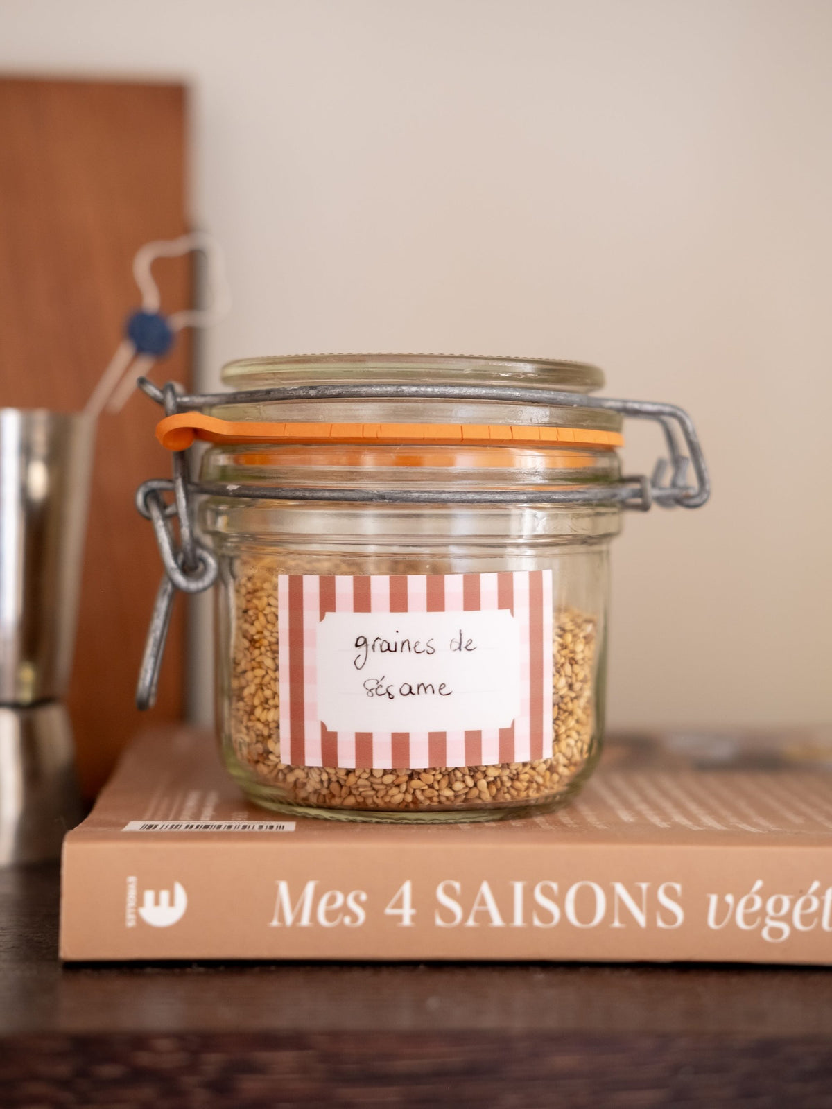 Étiquette adhésive à rayures rouges et blanches, marquée « graines de sésame », collée sur un bocal en verre.