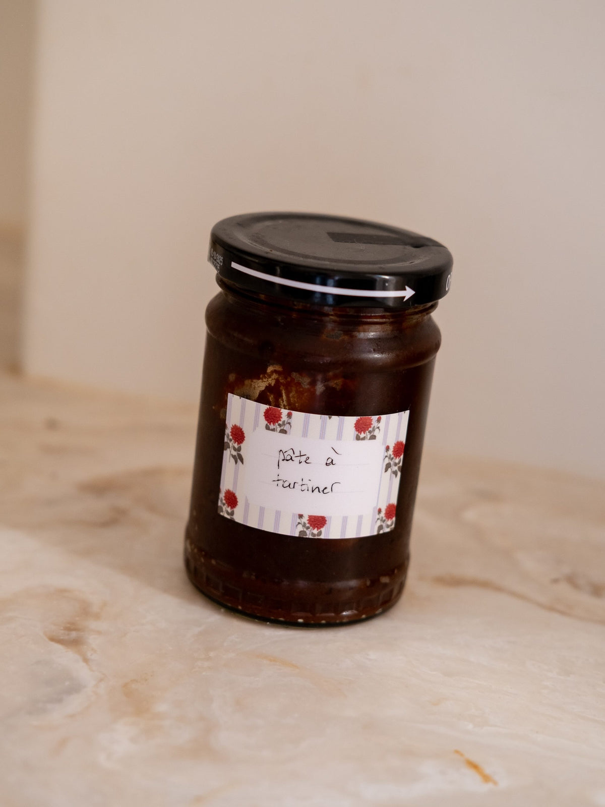 Étiquette adhésive à fleurs rouges et rayures claires, marquée « pâte à tartiner », collée sur un pot en verre.