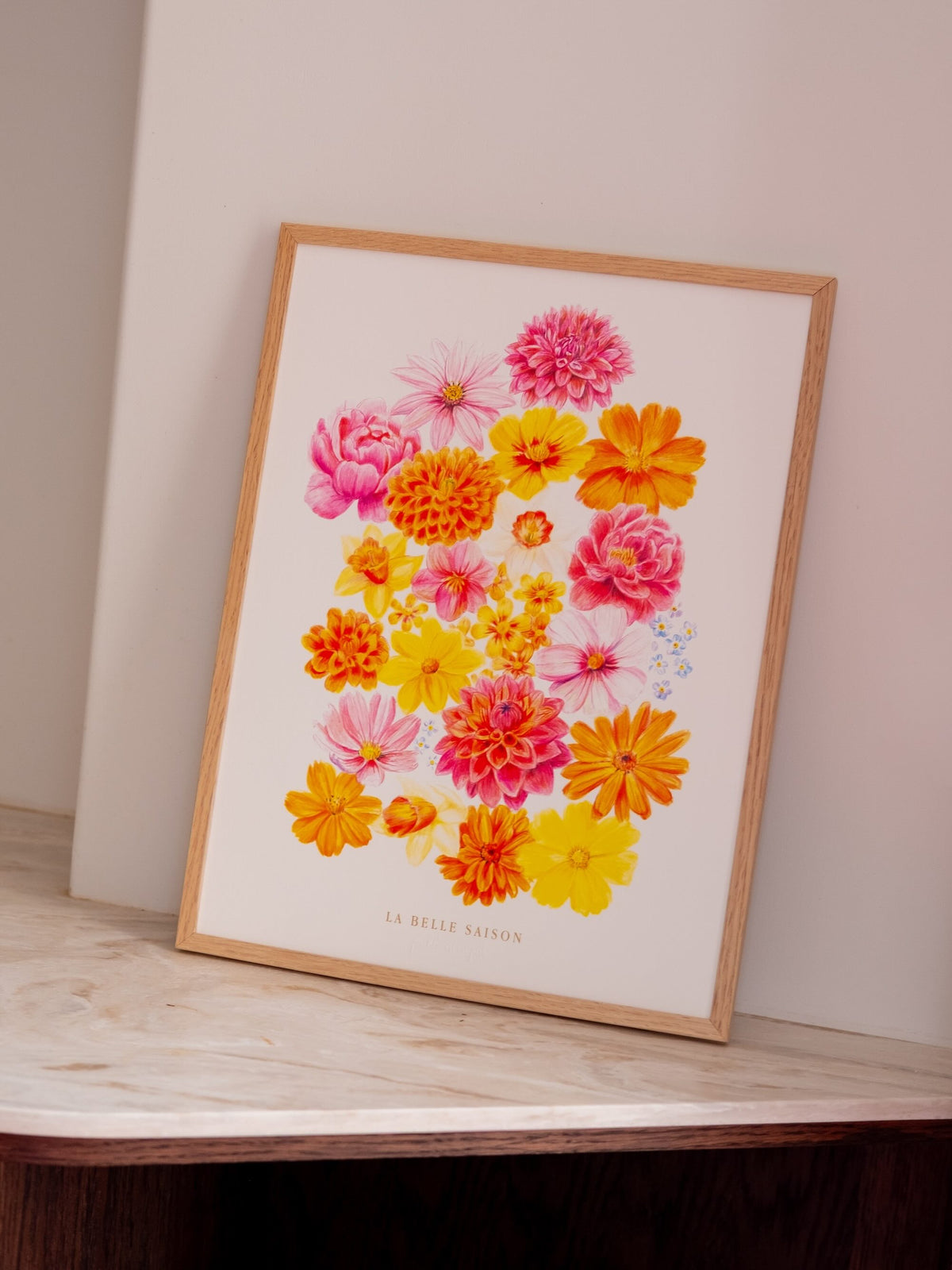 Affiche florale « La Belle Saison » aux fleurs roses, jaunes et orange, dans un cadre en bois sur du marbre clair.