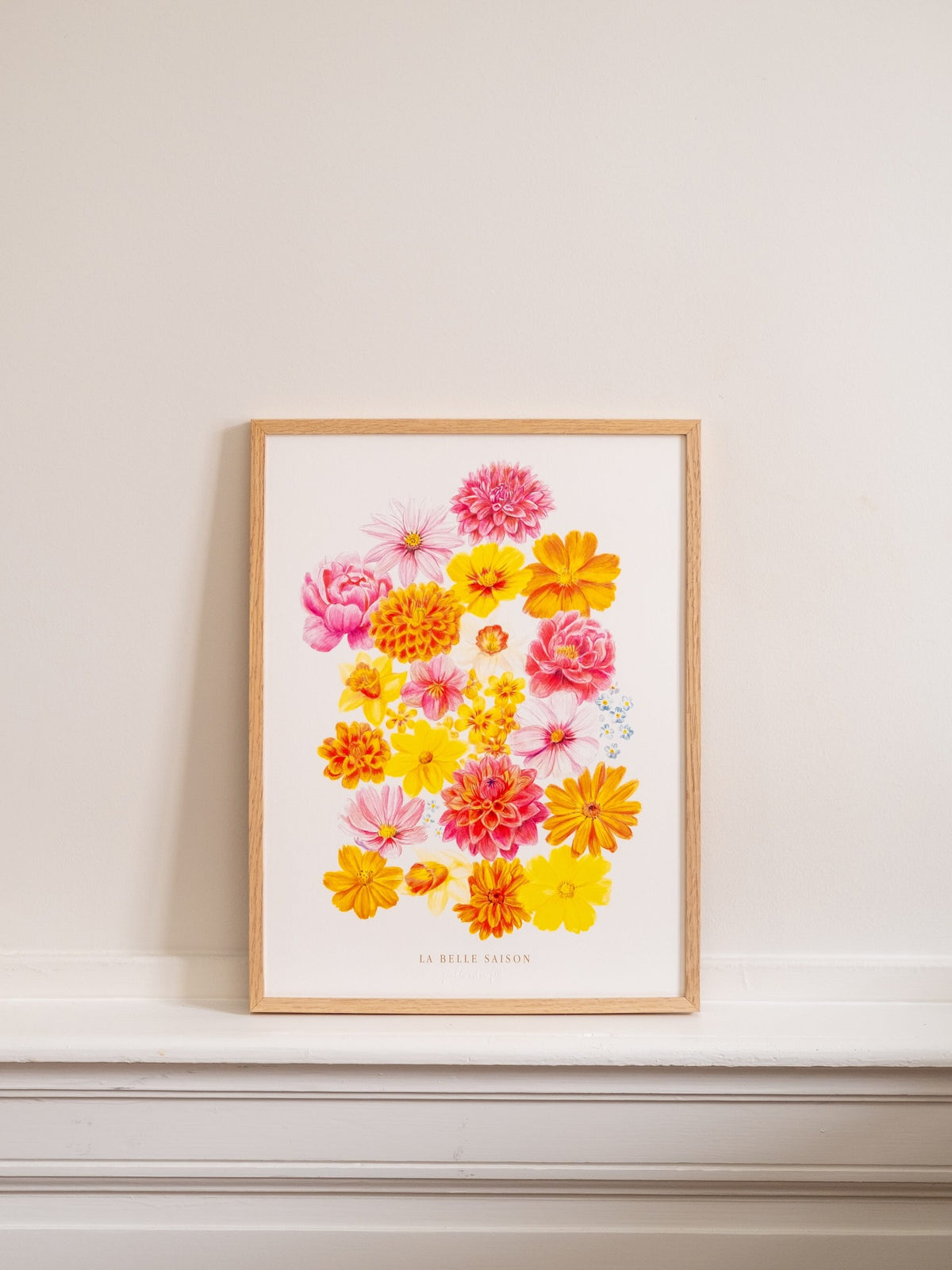 Affiche florale « La Belle Saison », présentée de face dans un cadre en bois clair sur une cheminée blanche.