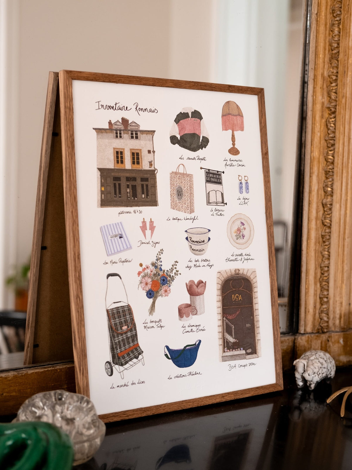 Affiche Inventaire rennais illustrant des boutiques et objets de Rennes, encadrée devant un miroir ancien.