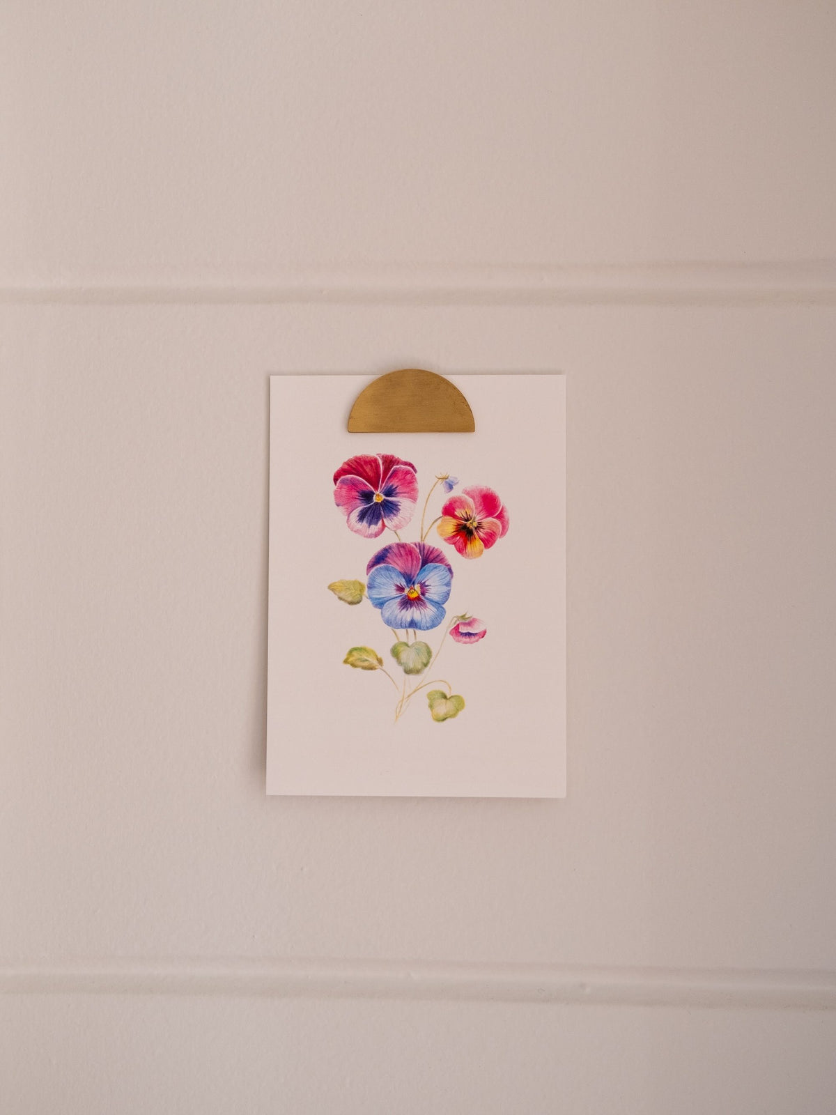 Carte postale illustrée de pensées multicolores, fixée sur un mur clair avec une pince dorée.